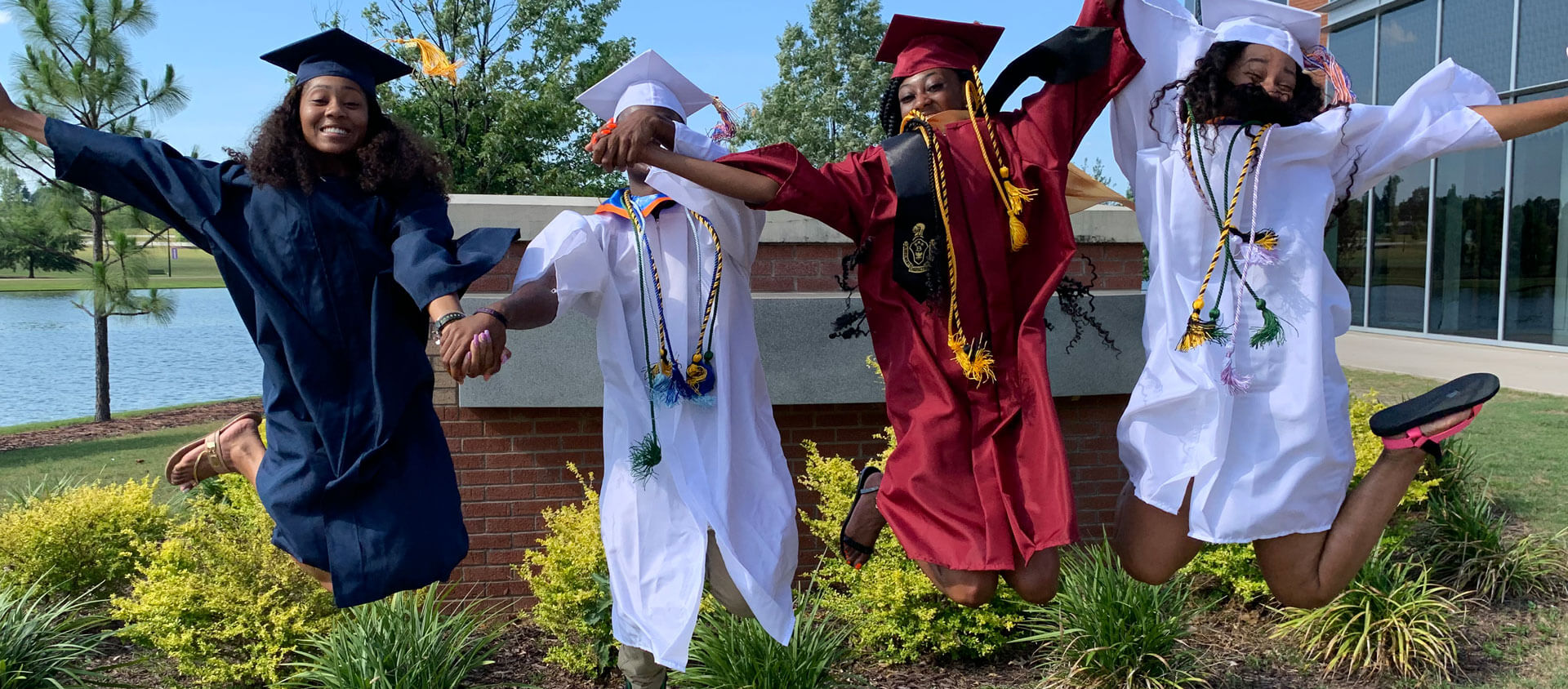 graduates holding hands and jumping in the air